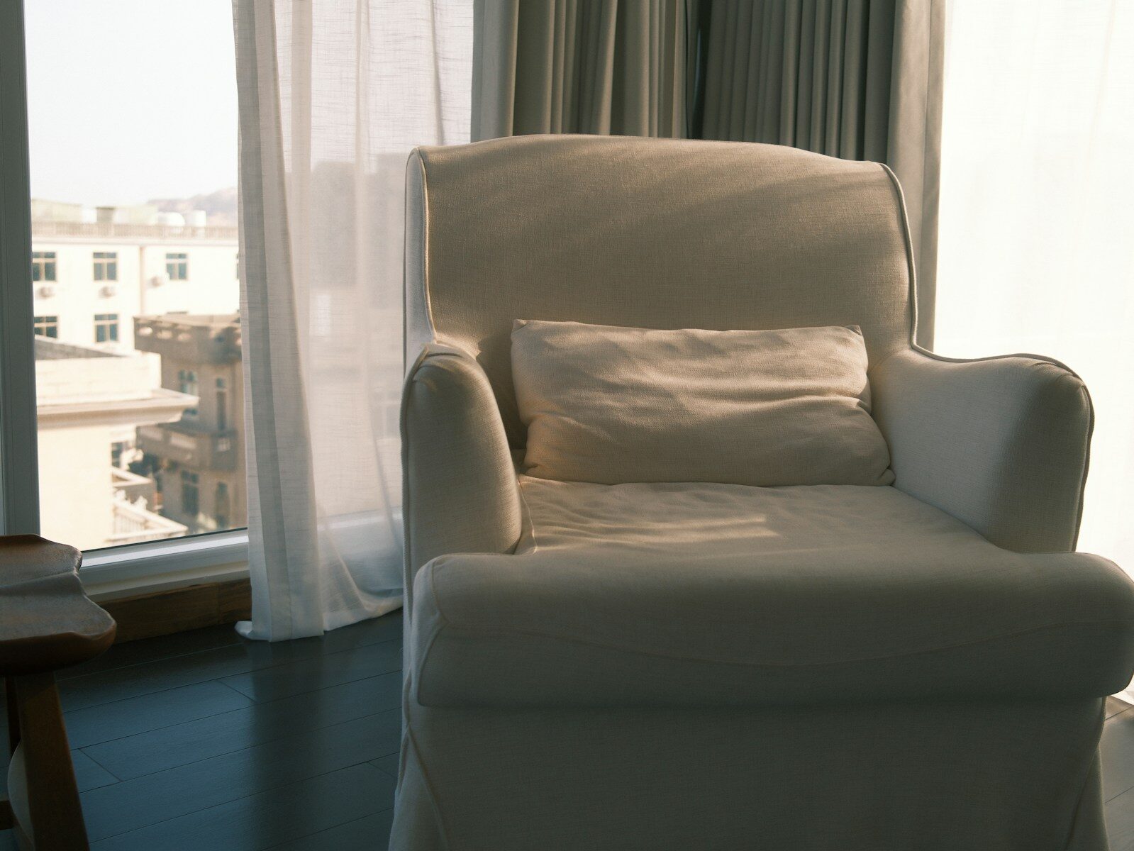 A white armchair with a pillow by the window.